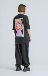 Remera negra con efecto nevado, corte oversize, mangas cortas y cuello redondo. Estampado en la espalda con diseño de una figura femenina y la frase 'Chill Bitch Trust Karma - The Wheel of Fortune'.