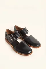 Zapato tipo oxford abierto en los laterales, confeccionado en cuero vacuno negro. Presenta doble tira con hebillas metálicas en el empeine y detalle de tachas plateadas en el contorno del talón y la puntera.