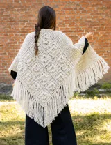 Ruana artesanal tejida en crochet con diseño de cuadrados con flores en relieve. Presenta un corte triangular con flecos largos en todo el borde inferior, ofreciendo una caída envolvente y texturizada.