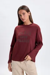 Remera de manga larga en color bordó, con cuello redondo y estampa frontal con la inscripción 'PARIS 1986 FRANCE' en estilo universitario.