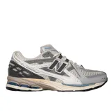 Championes New Balance modelo 1906, de estilo running urbano, con diseño técnico en tonos gris, plata y detalles en azul marino. Presenta una estructura de malla transpirable con refuerzos sintéticos, logo N lateral y entresuela con tecnología de amortiguación.