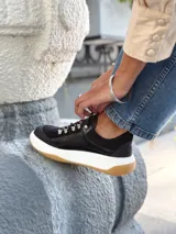 Zapatillas deportivas negras de cuero, con cordones y suela de goma blanca con base marrón.