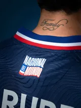 Camiseta de fútbol Umbro del Club Nacional de Football, modelo Away 2025, de color azul con patrón de ondas texturizadas. Cuenta con detalles en blanco, rojo y azul en el cuello y las mangas. Incluye el escudo del club, el logo de Umbro y patrocinadores estampados.