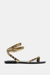 Sandalia plana dorada con tiras finas con tachas metálicas en forma de conchas. Tiene tira trasera al tobillo con cierre de hebilla metálica.