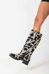Botas de caña alta con estampado de vaca en blanco y negro, con tacón bajo y puntera redondeada.