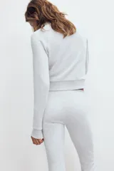 Chaqueta de felpa color gris claro melange, con cuello solapa, manga larga con puños elastizados, bolsillos frontales y cierre de cremallera completa.