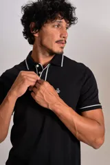 Polo de manga corta confeccionado en tejido interlock suave, color negro con detalles de vivos en color blanco en el cuello y las mangas. Presenta tapeta con botones y un bolsillo frontal con el logo bordado.