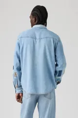 Camisa de jean estilo western con diseño de parches tipo sashiko en las mangas. Presenta cuello clásico, cierre frontal con botones a presión, dos bolsillos en el pecho con solapa y puños abotonados.