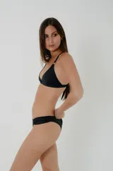 Conjunto de bikini negro con soutien triangular que incluye argollas metálicas en el escote y en la unión con los breteles, acompañado de una bombacha clásica con laterales finos.