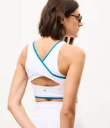 Top deportivo femenino confeccionado en microfibra, de color blanco con vivos en azul, escote redondo, copa y breteles anchos.