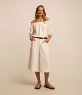 Blusa de tricolina blanca con estampado de lunares dorados en foil, escote descubierto estilo hombro a hombro y mangas largas abullonadas con puños elásticos.