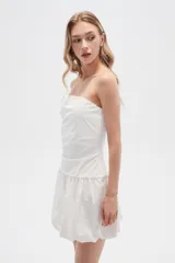 Vestido corto strapless de color blanco, con diseño drapeado en el torso y falda estilo globo con ruedo voluminoso.