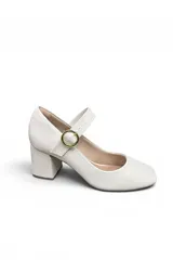 Zapato tipo Mary Jane de color blanco, con taco cuadrado medio y tira en el empeine con hebilla metálica dorada circular.