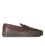Championes tipo mocasín Vans, confeccionados en cuero marrón con diseño inspirado en el skate. Presentan una construcción vulcanizada con suela waffle, detalles de tachuelas en la lengüeta y adornos metálicos removibles.