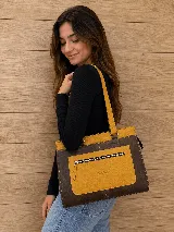 Cartera de cuero marrón de tamaño medio con diseño estructurado, que combina cuero liso y un panel frontal texturizado tipo cocodrilo con bolsillo exterior con cierre. Cuenta con doble asa de hombro y costuras visibles de contraste.