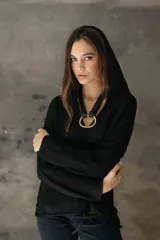 Sweater de punto negro con capucha, diseño de manga larga y corte holgado. Presenta un detalle de argolla metálica en el escote.