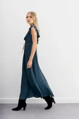 Vestido largo negro de escote redondo con volados decorativos que recorren el frente y la espalda. Presenta un cordón de ajuste en la cintura con terminaciones metálicas y espalda baja.