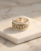 Anillo ancho de acero con baño de oro, compuesto por múltiples bandas texturizadas y una banda central engastada con circonias brillantes.