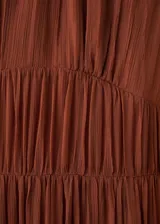 Vestido midi marrón de viscosa transparente, con diseño plisado, cuello alto fruncido y mangas largas abullonadas con puños elásticos. Presenta detalles de costuras fruncidas en la cintura y falda escalonada con vuelo.