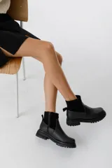 Bota corta de cuero color marrón claro (visón) con caña arrugada y suela track negra gruesa. Presenta un detalle de tira de cuero con hebilla en el tobillo.