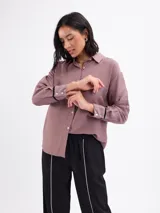 Camisa de manga larga color malva, con cuello clásico, cierre frontal con botones y detalles de vivos negros en los puños.