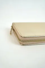 Billetera rectangular con cierre perimetral de cremallera, de color dorado con acabado metalizado y textura sutil.