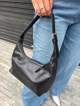 Cartera tipo baguette de cuero sintético color negro, con diseño curvo, cierre superior y asa corta regulable con hebilla metálica.