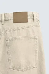 Pantalón jeans de corte recto y tiro medio, confeccionado en denim de algodón color beige con efecto lavado, bolsillos clásicos y cierre frontal con cremallera y botón.