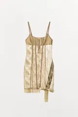 Vestido corto semitransparente tipo corsetero color beige, confeccionado con encaje y detalles de varillas interiores que estilizan la figura. Presenta escote redondo, tirantes finos ajustables y bajo asimétrico con una lazada lateral de satén.