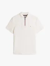 Chomba de corte regular de Tommy Hilfiger, color blanco, con cuello polo y cierre de cremallera de 1/4. Cuenta con mangas cortas y detalle del logo bordado en el pecho.