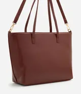 Cartera tipo shopper grande de Satinato, confeccionada en poliuretano con textura efecto crocco en color marrón. Presenta doble asa fija, correa larga desmontable con herrajes dorados y cierre superior por cremallera.