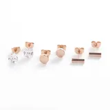 Set de tres pares de aros mini color oro rosa en acero quirúrgico: un par con forma de cubo con cristal, un par con forma circular y un par con forma de barra horizontal.