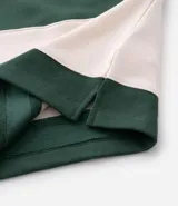 Chomba de manga larga con cuello polo y cierre frontal con botones. Presenta un diseño de rayas horizontales anchas en bloques de color verde y beige. Confeccionada en tejido de algodón de alta calidad.