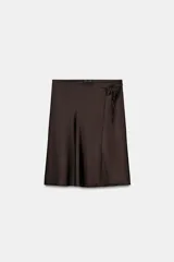 Falda corta tipo pareo, color marrón oscuro, confeccionada en tejido satinado con lazada ajustable en el lateral.