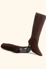 Bota de caña alta confeccionada en gamuza color marrón, con diseño minimalista, punta fina y taco kitten heel de 6 cm.