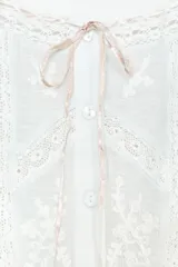 Top corto blanco de gasa con escote cuadrado, mangas cortas y bordados de flores en el frente. Presenta lazada a contraste en escote y mangas, y cierre frontal con botones.