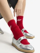 Zapatillas Adidas Samba Jane W de color plateado, con diseño híbrido entre zapatilla y Mary Jane, confeccionadas en piel y material sintético. Presentan tres bandas laterales blancas, tira ajustable con cierre de velcro en el empeine, y suela de goma de tipo caramelo.