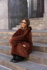 Canguro unisex color marrón chocolate de tela suave con capucha y bolsillo tipo canguro. Tiene un logo pequeño en la parte inferior. Se puede usar largo o corto ajustando la piola.