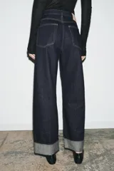 Jeans de tiro medio con corte baggy y pierna relajada. Presenta diseño de cinco bolsillos, cierre frontal con cremallera y botón, y bajo con vuelta marcada.