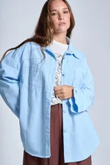 Sobrecamisa color beige confeccionada en gabardina, de corte holgado, con cuello camisero, cierre frontal con botones, dos bolsillos de parche en el pecho y mangas largas con puños abotonados.