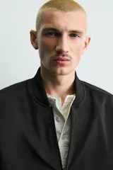 Cazadora bomber ligera de tejido técnico color verde oliva, con cuello, puños y bajo en rib elástico. Presenta cierre frontal de cremallera y bolsillos de vivo en la cadera.