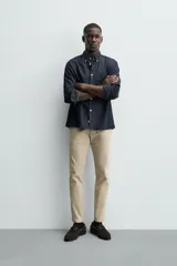 Pantalón chino de corte ajustado, color beige, con bolsillos laterales y bolsillos traseros de vivo. Cuenta con cierre frontal de cremallera y botón.