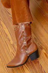 Bota estilo tejana de cuero vacuno color chocolate, con detalle de tachas metálicas en el lateral externo, cierre interno y taco cuadrado negro.