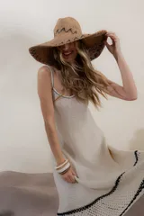Vestido tejido de algodón y poliéster color crema, de corte largo y tirantes finos. Presenta un borde inferior con terminación artesanal en crochet con dibujo de calados en hilo negro.