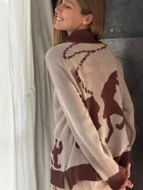 Campera de punto color beige con cuello polo marrón, cierre frontal y puños acanalados. Presenta un diseño con motivos ecuestres en color marrón en la parte trasera.