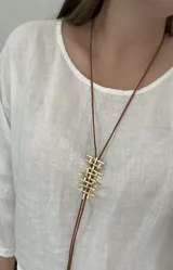 Collar largo con tiento de cuero marrón y dije de bronce con diseño de rejilla.