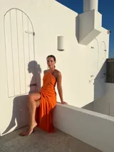 Vestido largo naranja de crepé con escote en pico y falda tipo pareo regulable.