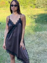 Vestido tipo lencero de seda natural con corte asimétrico, escote en V y ruedo decorados con encaje negro. Presenta breteles finos ajustables y una caída fluida y holgada.