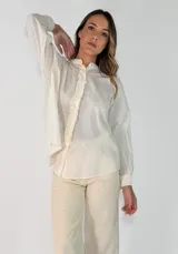 Camisa de algodón de corte holgado, con cuello mao y detalle de volados verticales a lo largo de la botonadura frontal. Presenta mangas largas con puños abotonados.