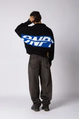 Campera tejida de punto con cierre frontal completo y cuello polo. Presenta un diseño con franja horizontal en color azul y letras en blanco sobre fondo negro, con puños y ruedo acanalados.